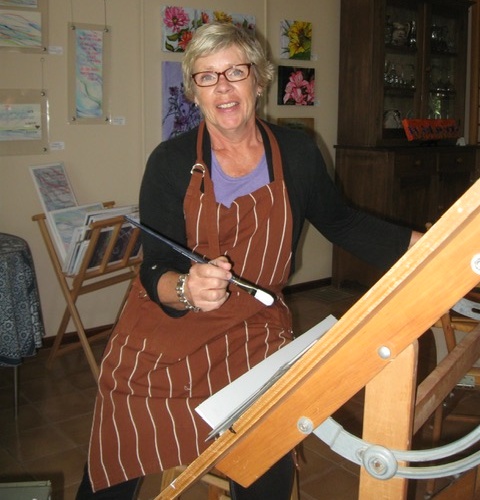 Judith Gould smiling in her art studio holding a paintbrush at her easel